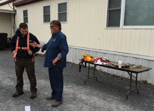Jake Rhoades, an ARC master plumber, dons a harness at the fall protection station while the instructor, Lonny Wade, Catamount Safety, discusses the proper way to wear it.